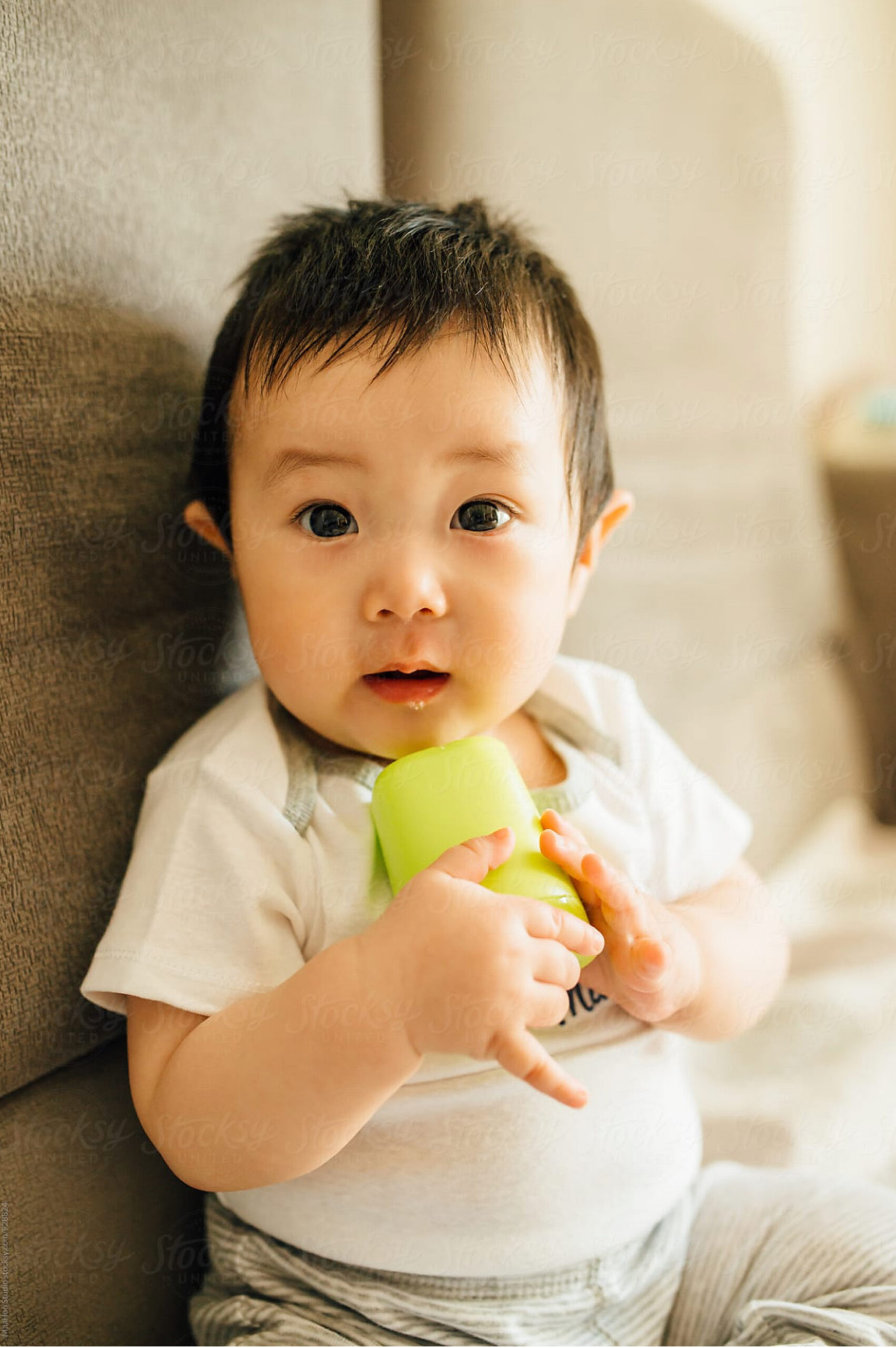 Baby with short black hair sits against a beige background