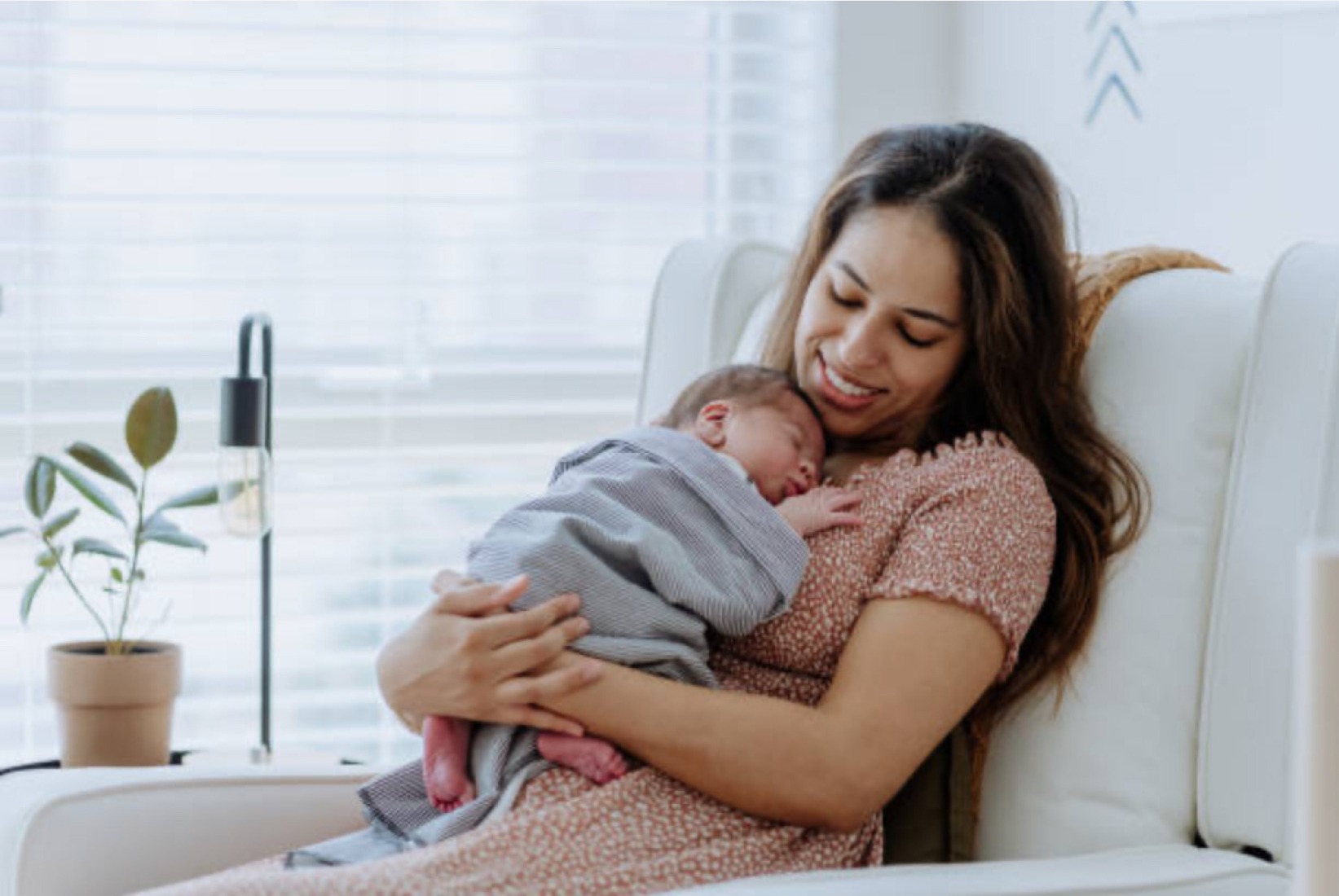 A mother joyfully cradles her sleeping newborn in a cozy chair