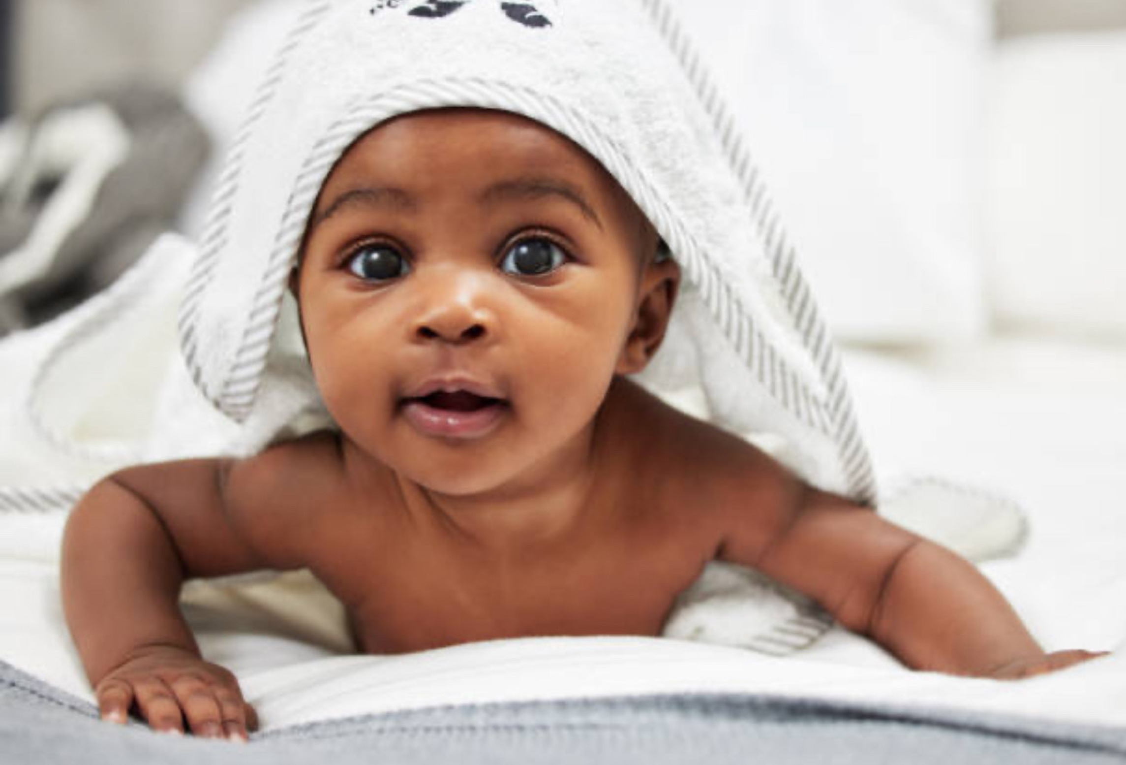 A baby with big, bright eyes is lying on a soft blanket