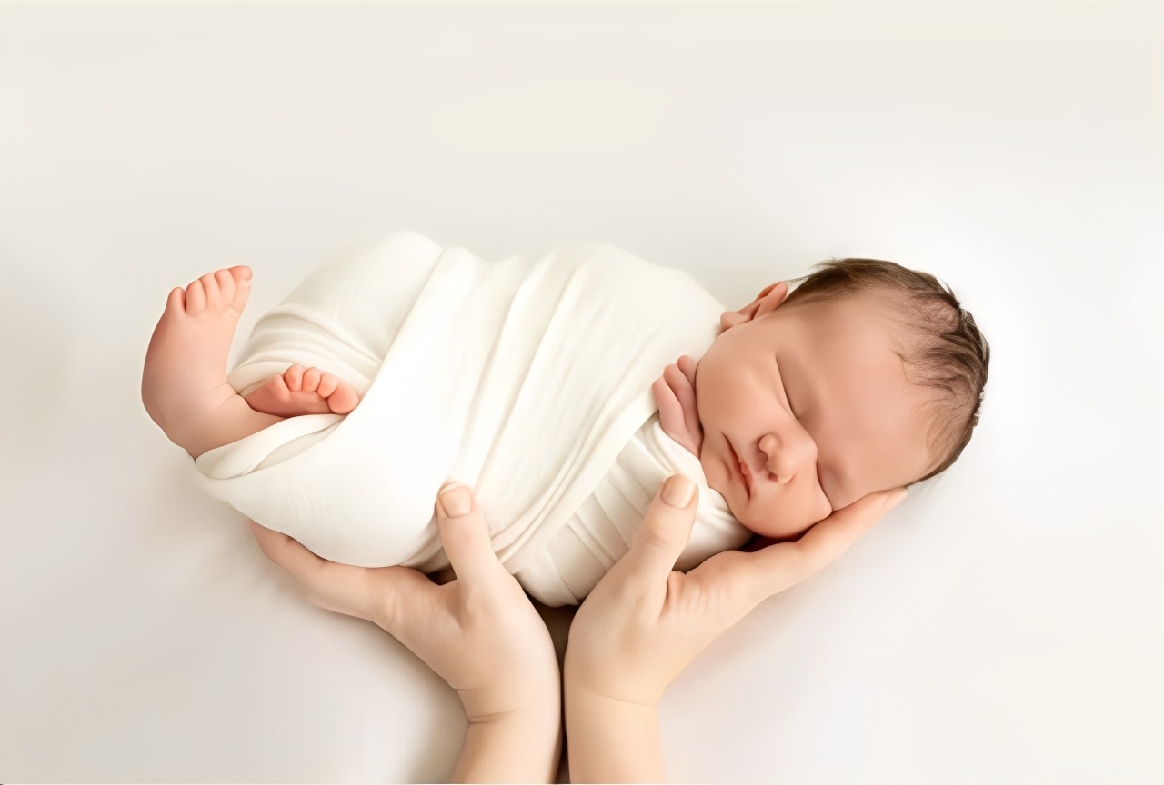 A sleeping baby in a light pink onesie lies peacefully beside a woman